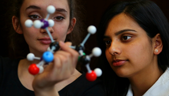Women looking at atom - stock image