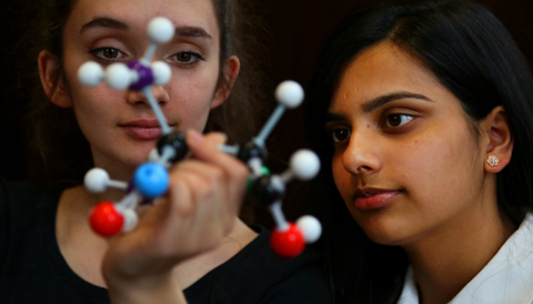 Women looking at atom - stock image